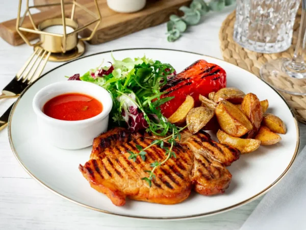 Saftiges gegrilltes Schweinefleisch in Tomatensoße mit Bratkartoffeln